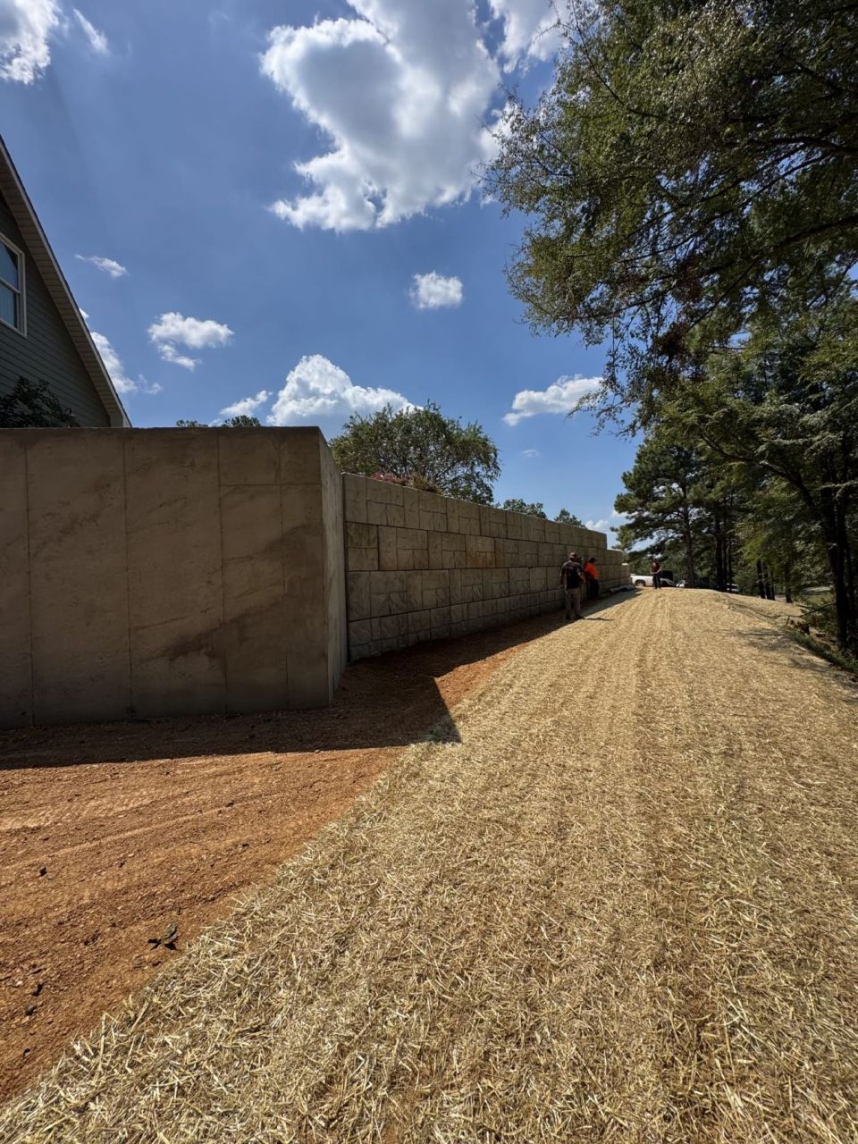 Finished concrete block retaining wall along a new gravel driveway with a straw-covered shoulder