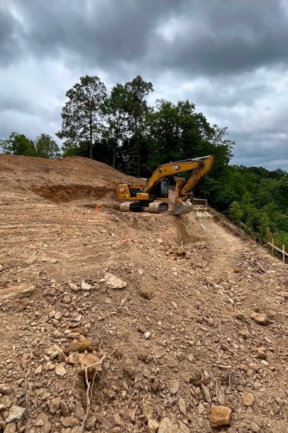 Excavator cutting into a red clay hillside to prepare a retaining wall site