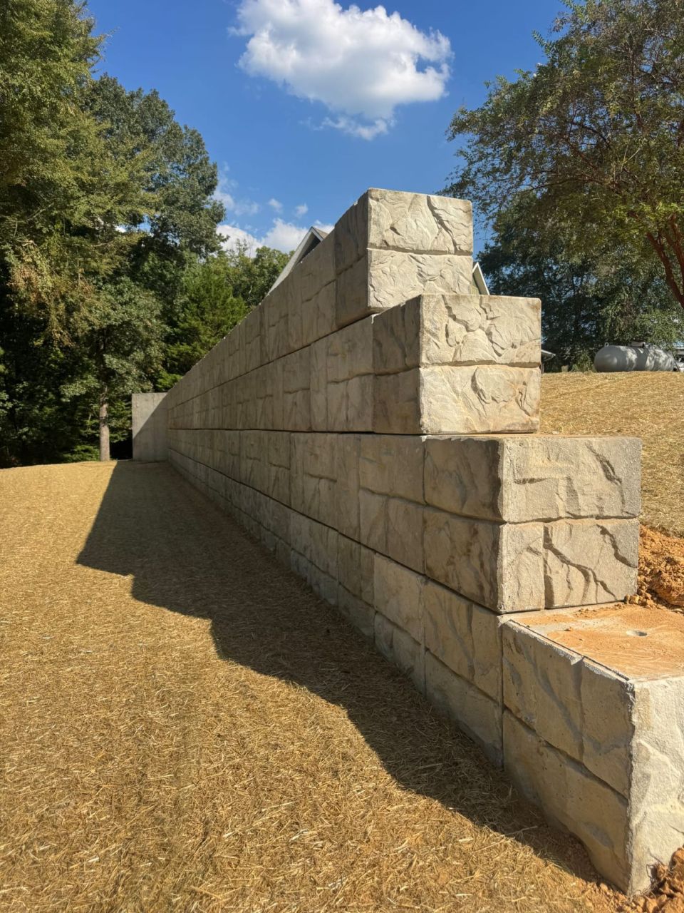 Stepped end of a concrete block retaining wall with a straw-covered, seeded slope