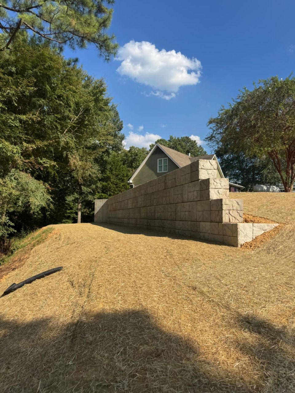 Stepped concrete block retaining wall finished with straw and seed next to a house