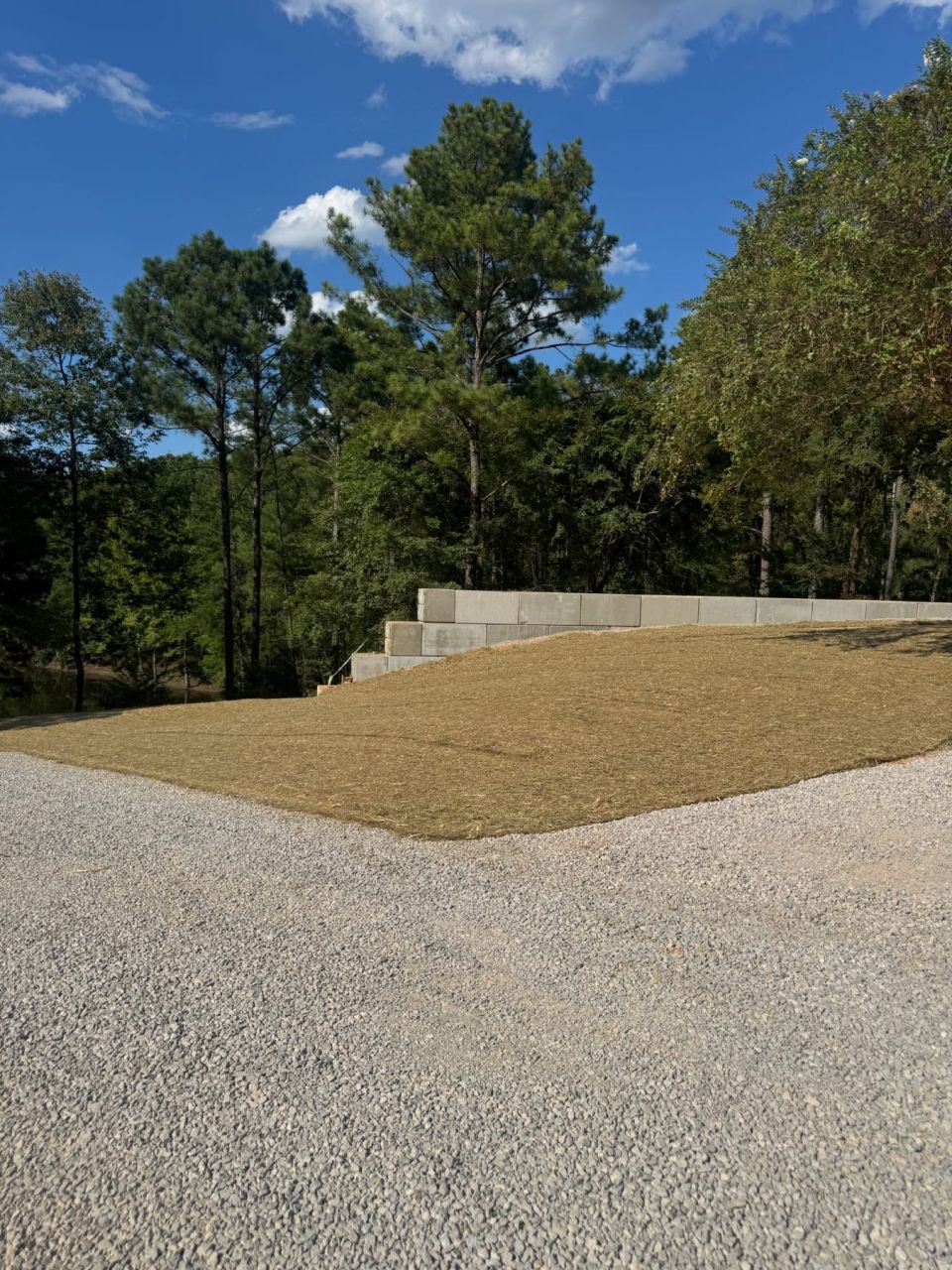 Seeded, graded yard above a low concrete block retaining wall and a gravel parking area