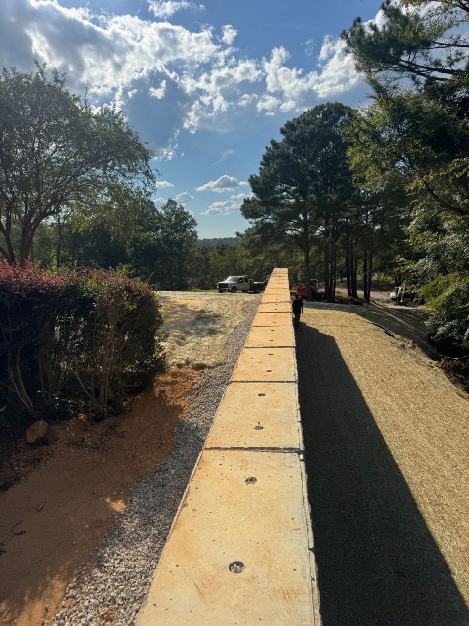 Top of a long concrete block retaining wall beside a gravel drive and a seeded slope